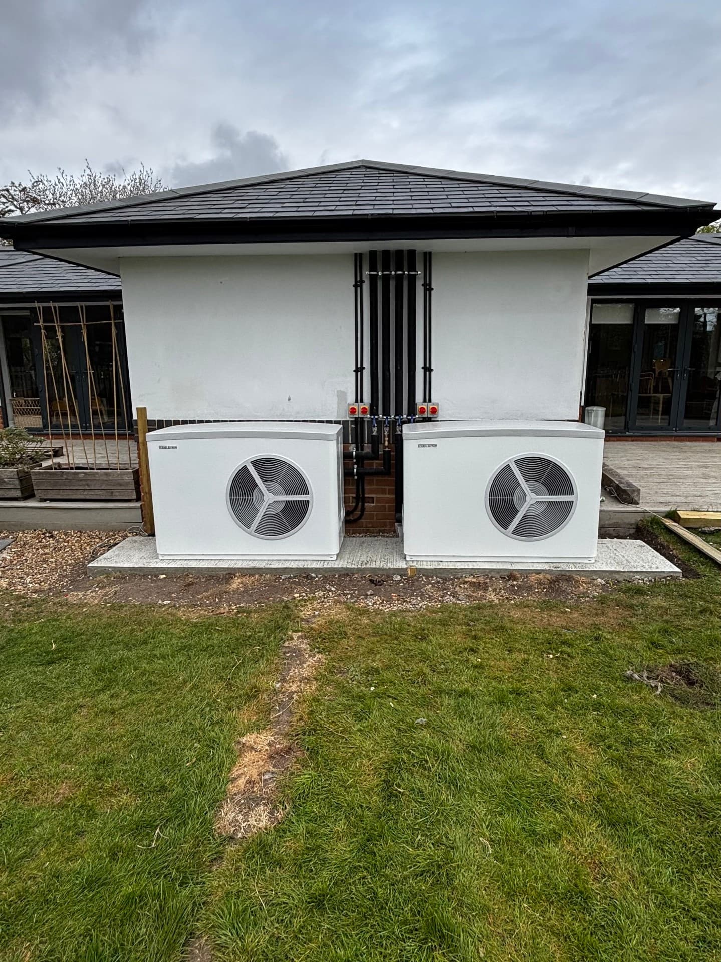 Two air source heat pumps on a concrete base outside a property